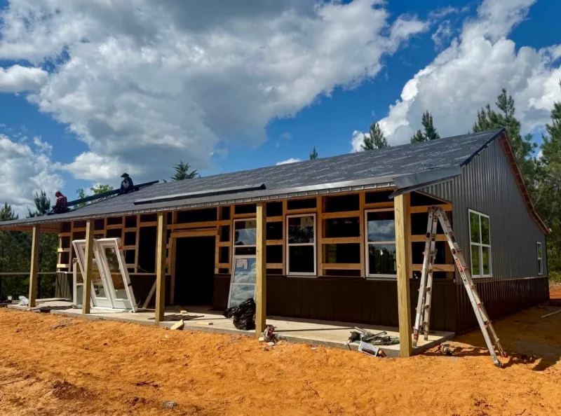 Crew roofing a two-tone barndominium with the porch framed and windows going in