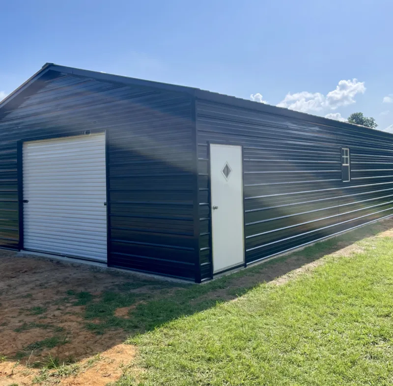 Blue metal garage with a white roll-up door and walk door on a lawn
