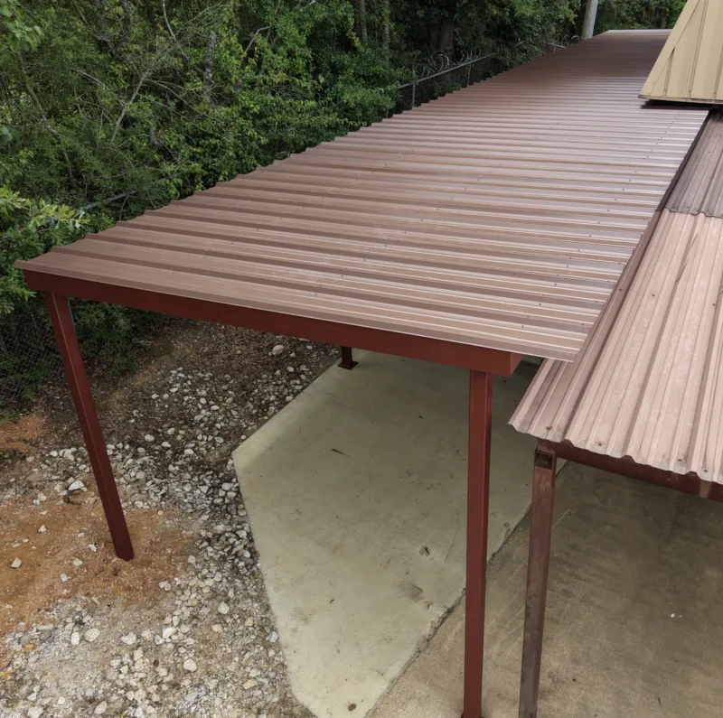 Brown metal lean-to over a concrete slab at the edge of the woods