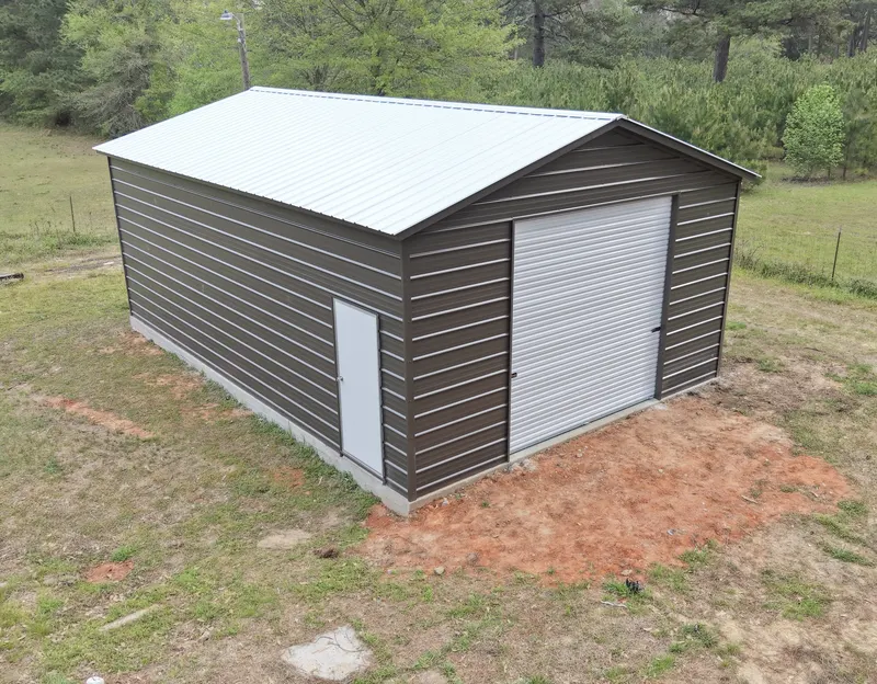 Brown metal shop building with a white roof and roll-up door on a cleared rural lot