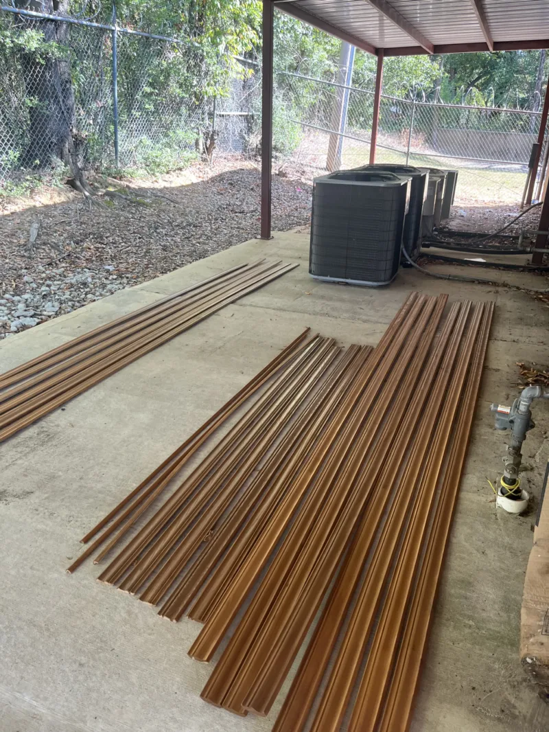 Bundles of trim and HVAC units staged under a carport for an office build-out