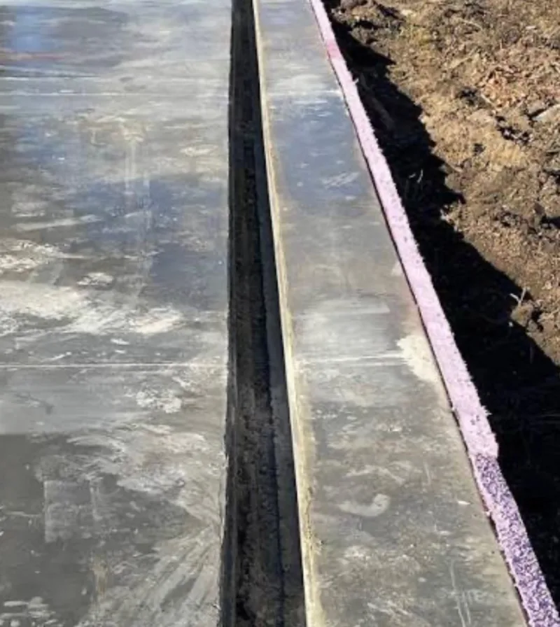 Close view of a channel formed between a concrete slab and a curb, with a pink foam strip along the outer edge of the curb