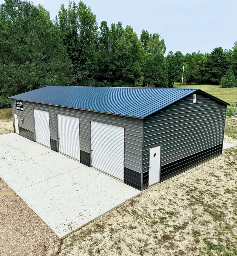 Charcoal metal building with a blue roof and four roll-up doors on a new slab