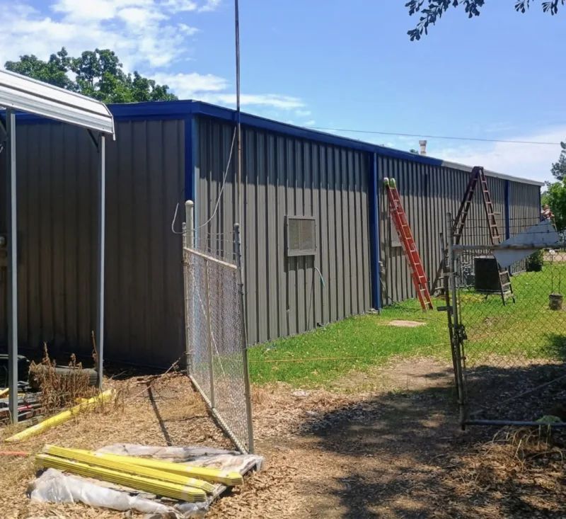Grey metal commercial building with blue trim behind a chain-link fence