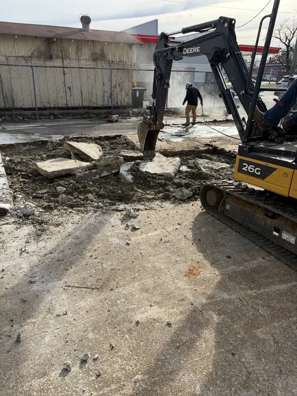 Compact excavator breaking out old concrete at a commercial site