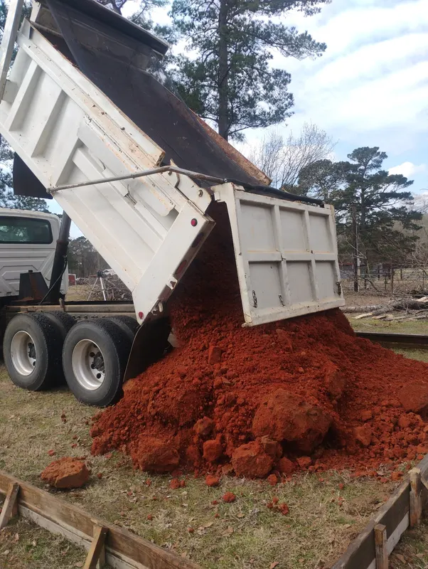Dump truck tipping red fill dirt beside a formed building pad