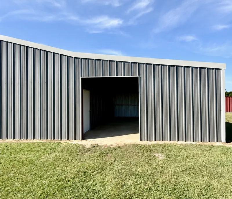 Grey metal shop building with an open bay door on a mown lawn