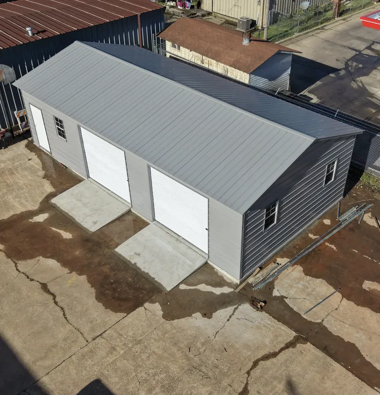 Grey and white metal garage with three roll-up doors and poured concrete ramps