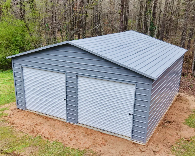 Grey metal garage with two white roll-up doors on a fresh dirt pad