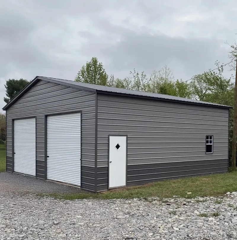Grey two-tone metal garage with two roll-up doors and a walk door on gravel
