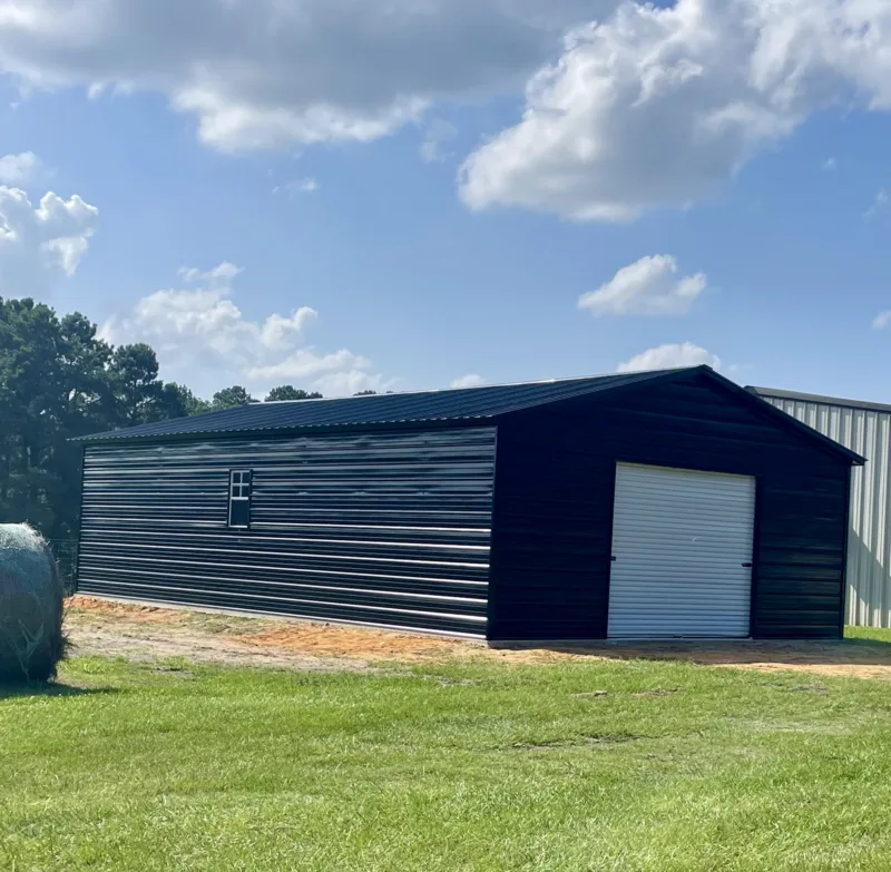 Navy metal garage with a white roll-up door beside a pasture
