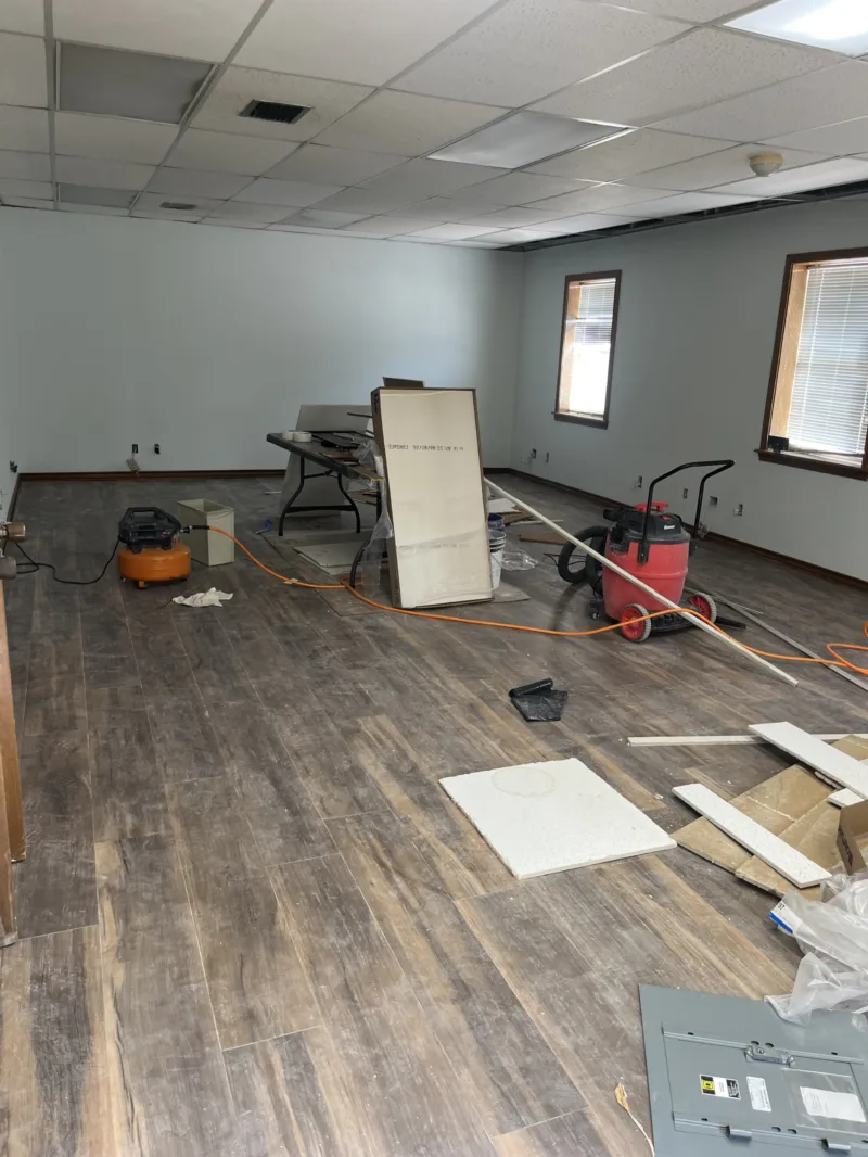 Office room mid-renovation with new plank flooring and tools on the floor