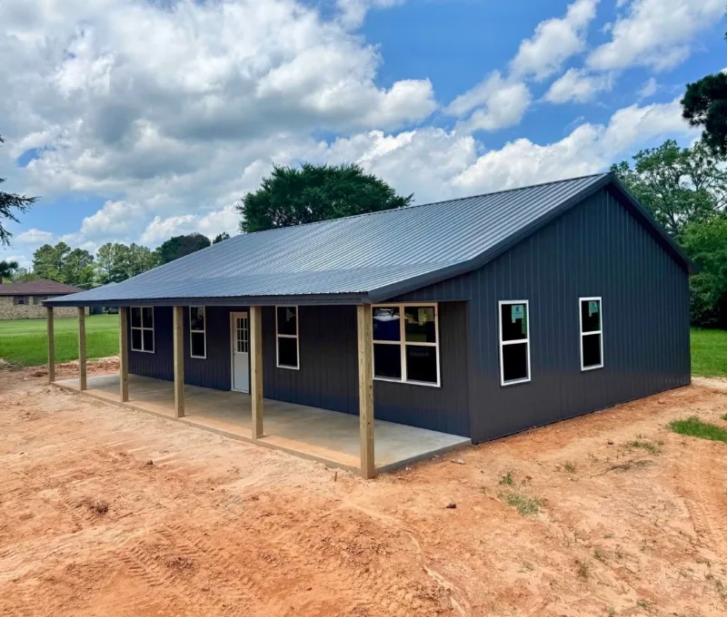 Charcoal post-frame home with a full-length covered porch on a fresh dirt lot