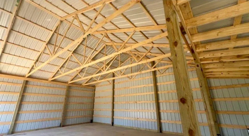 Inside a post-frame building with wood trusses, girts and white steel liner panels