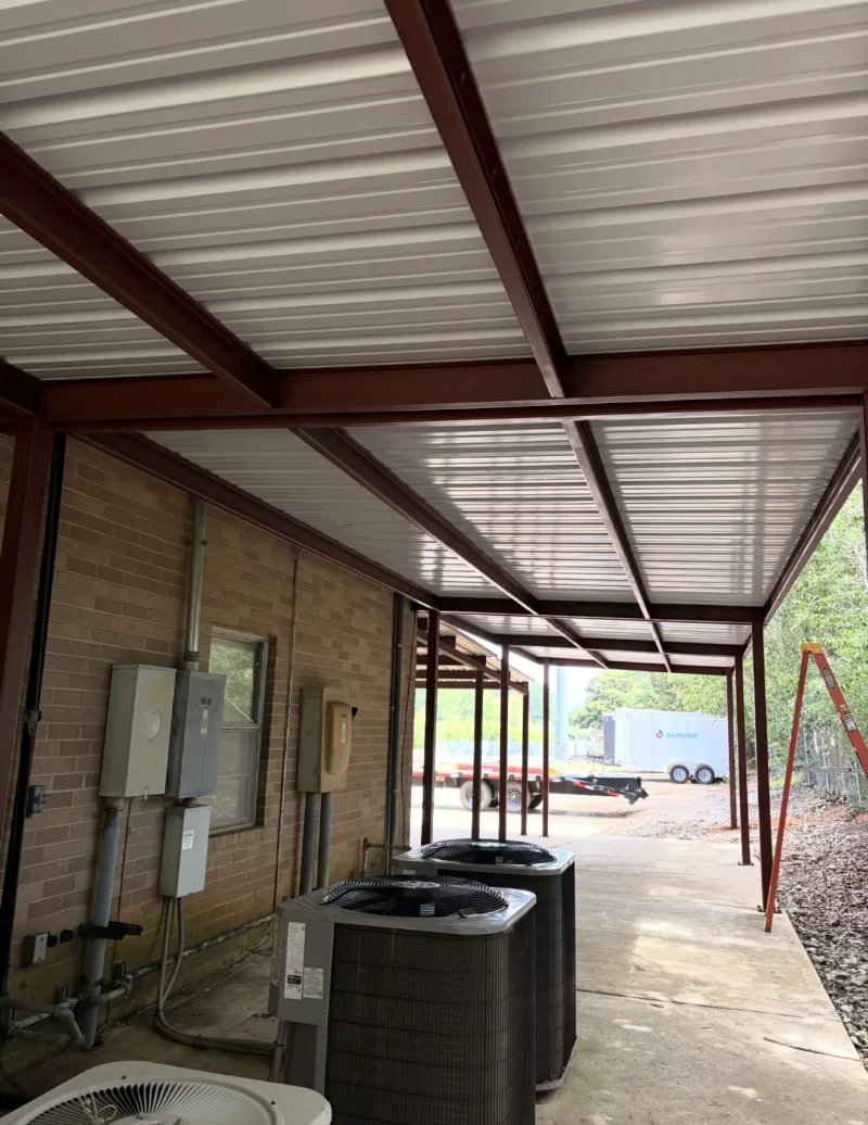 Red iron covered walkway along a brick building, with AC units beneath