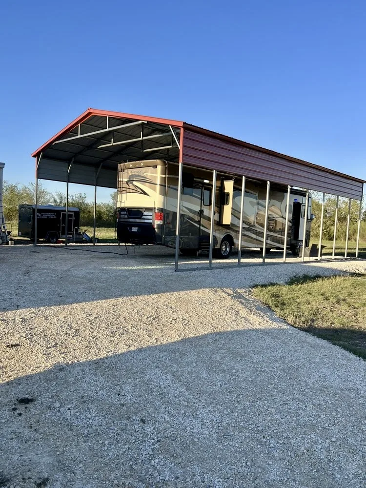 Red-roofed metal carport sheltering an RV on a gravel pad