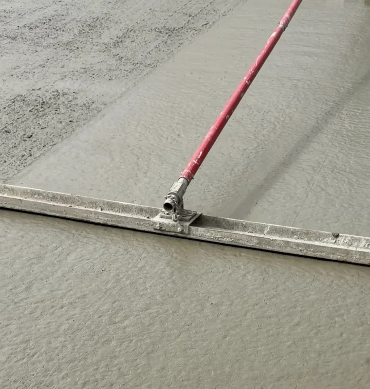 Screed bar levelling wet concrete across a fresh pour