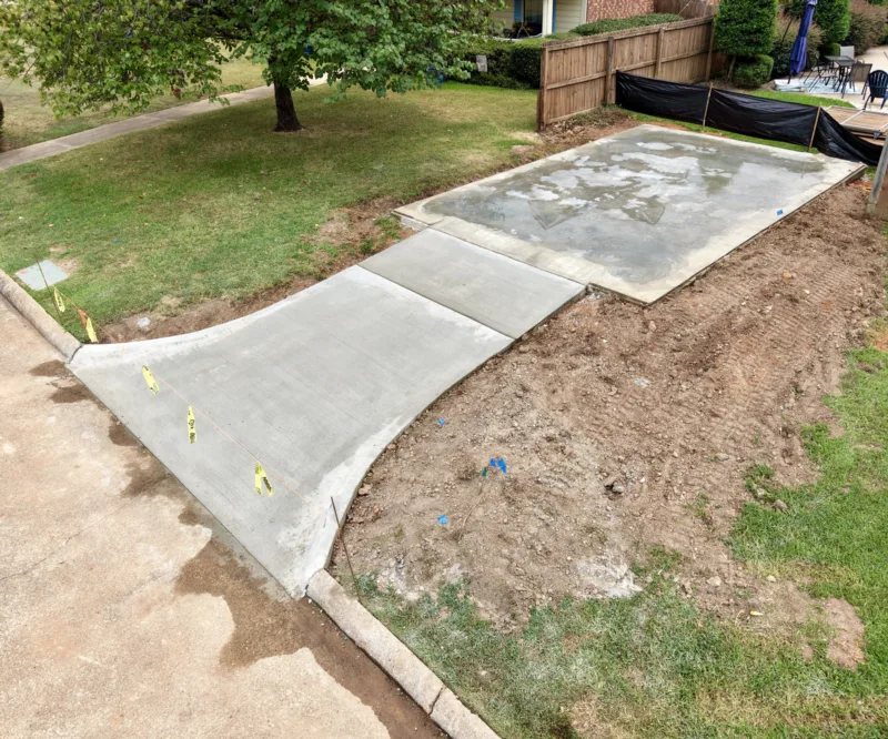 New concrete sidewalk leading to a poured pad in a backyard