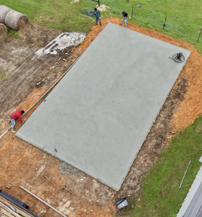 Crew finishing a long slab beside a hay field, seen from above