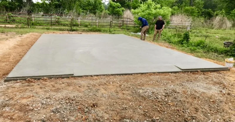 Two men checking a freshly finished slab beside a split-rail fence