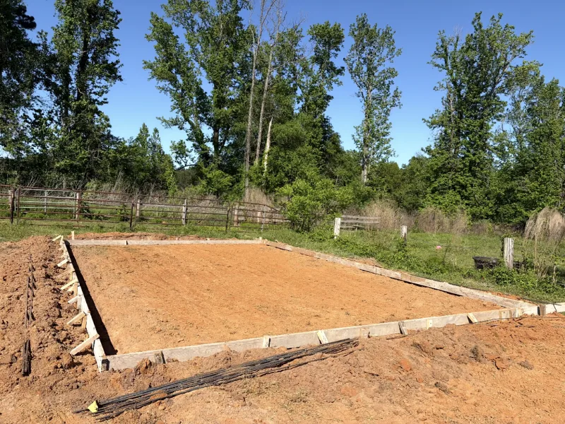 Wood forms set around a graded pad beside a split-rail fence