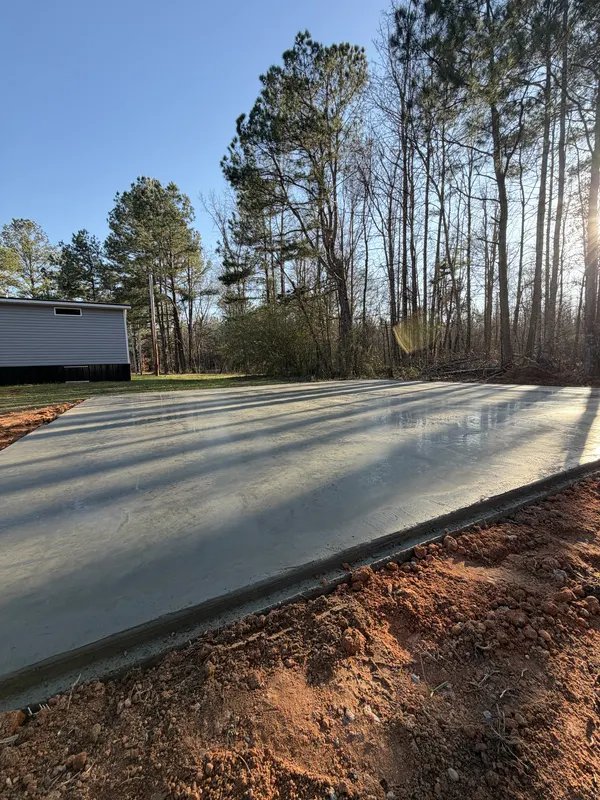 Freshly finished concrete slab catching low evening sun beside a house