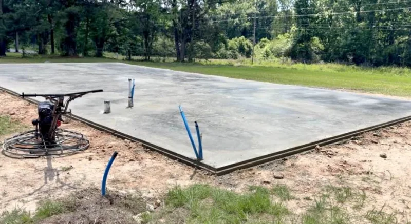 Fresh slab with plumbing stub-outs and a power trowel on it