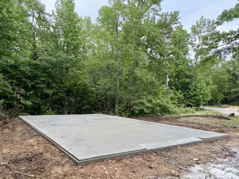 Finished concrete slab on a cleared pad at the edge of the woods