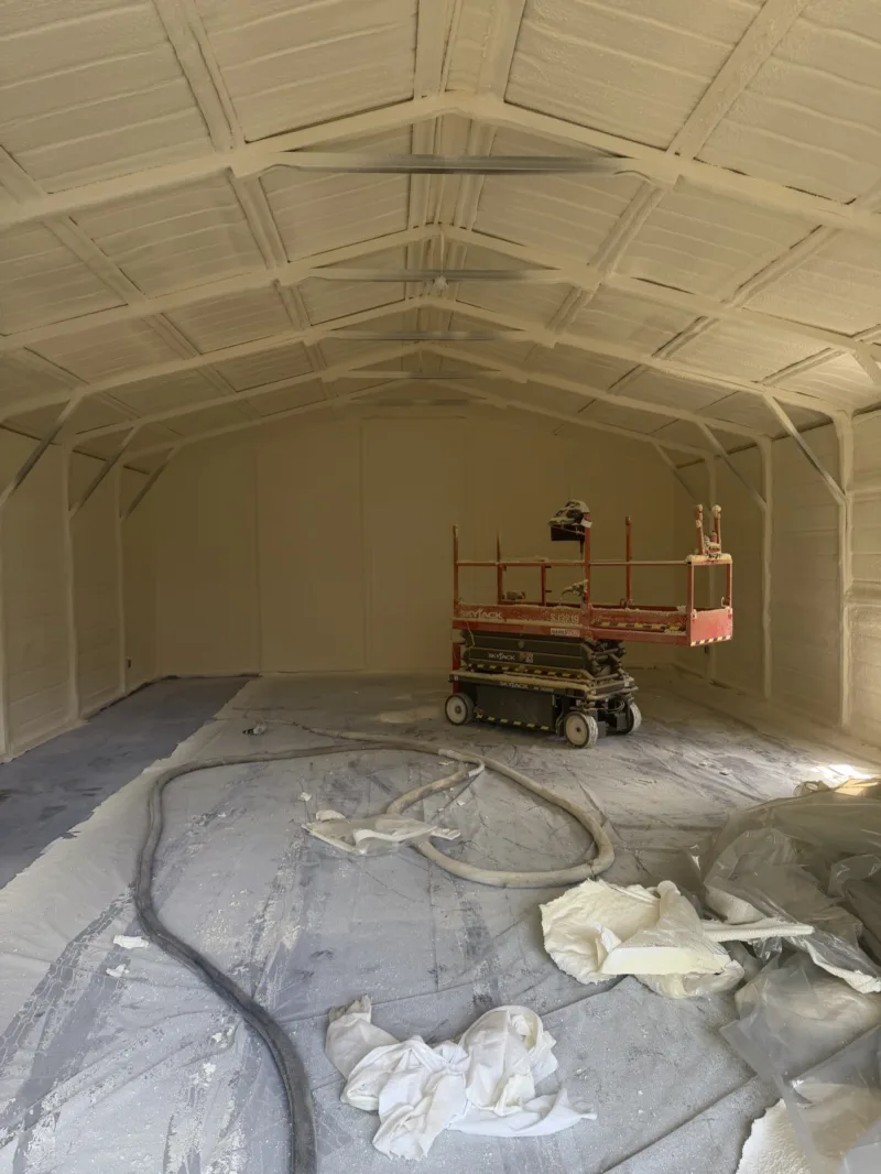 Metal building interior sprayed with foam insulation, a lift in the background