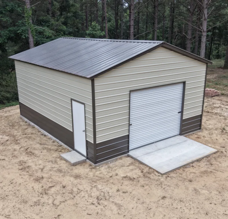 Tan metal garage with brown trim and wainscot on a sandy pad in the pines