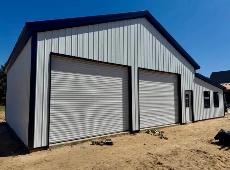 White metal shop with black trim, two roll-up doors, a walk door and windows